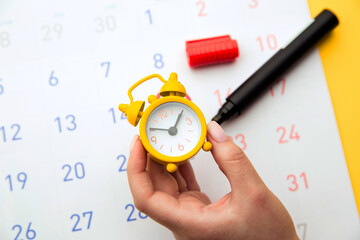 Young woman hand holding yellow clock. Calendar in background. Positive result. It is a time for baby.Gynecology concept.