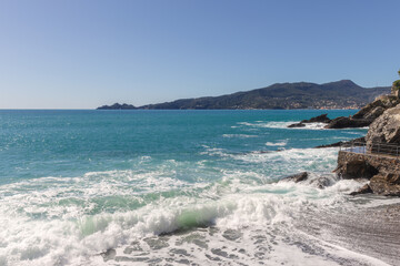 Waves crashing on rocks on a sunny day. On the background there is the promontory of Portofino