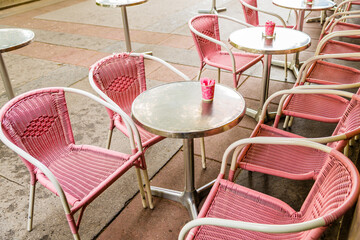 Fototapeta na wymiar Pink plastic wicker chairs and round silver tables with pink cups containing sugar outside a bistro. 