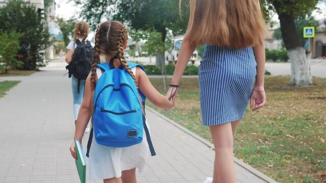 mom and daughter go to school. happy family school education concept. schoolgirl with mom go hand in hand lifestyle to school on footpath in the park. little girl with a briefcase time to study
