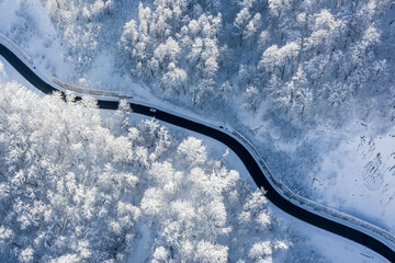Aerial top-down winter landscape of winding mountain road in a snow-covered forest lit by a rising...