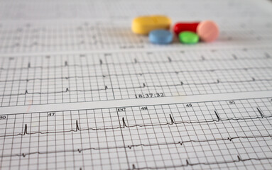 Colored pills on an electrocardiogram paper. Medications for cardiac patients. Heartbeats recorded on paper. Selective focus.