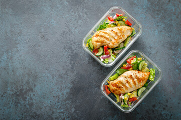 Lunch box containers with grilled chicken breast and fresh vegetable salad