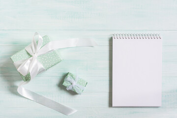Fototapeta na wymiar Gifts in a package with a white satin ribbon, a notebook on a wooden mint background. Top view, flat layout. The concept of a holiday, birthday, Mother's day. The composition is in pastel colors.