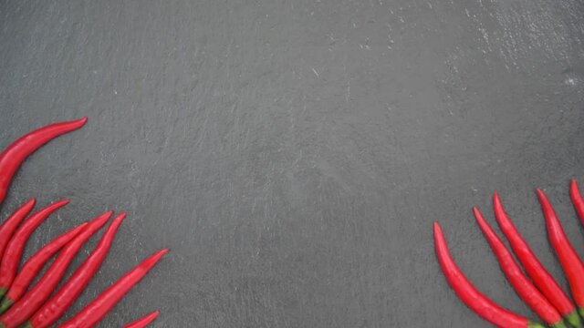 A female hand lays out a beautiful drawing with chili pepper. Black slate background. Background, texture.