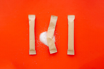 Sugar sticks in bright red backdrop, one torn apart with spilled white sugar. Sweet consumption,...