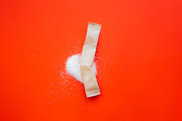 Broken paper stick with spilled sugar against vibrant red background. Abstract product photography, sugar and sweet consumption, copy space