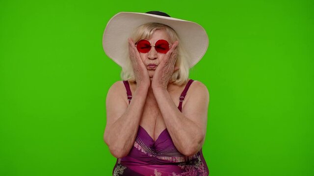 Funny silly senior pensioner woman tourist in swimsuit, fooling around making stupid face brainless dumb expressions on chroma key background. Portrait of old granny traveler model on summer vacations