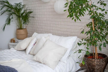 cozy bed with light linens and knitted blankets. Bright bedroom with lots of indoor plants and home decor.The concept of home comfort and recreation.