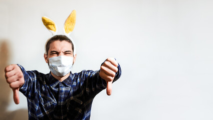 Celebrate Easter in coronavirus year with maximum protection and safety. Charming Caucasian man with beard yellow rabbit eared and protective medical mask puts on dislike with both hands.