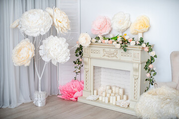elegant chic fireplace, the color of white chocolate, decorated with flowers and candles, and a light velour chair. Spring romantic decoration with a fireplace portal with artificial flowers.