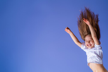 crazy excited little fun girl hanging happy upside down hands up on isolated purple studio background. Dynamic children's image. Emotions, expression. Copy space