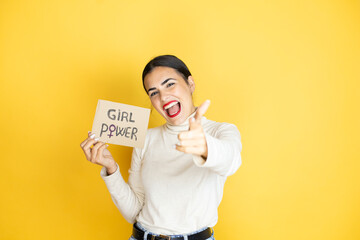 Young beautiful activist woman protesting holding poster with girl power message pointing to you and the camera with fingers, smiling positive and cheerful