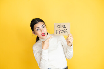 Young beautiful activist woman protesting holding poster with girl power message amazed pointing...