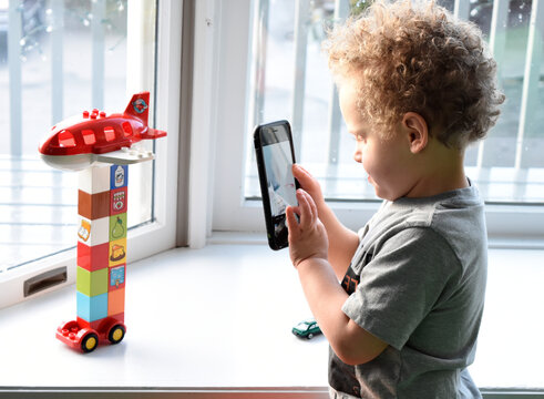 3 year old boy using cell phone to take pictures of his blocks creation.