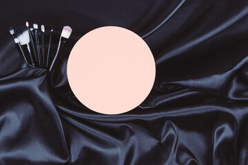 Make-up cosmetic brushes and pastel round blank podium platform on black wavy silk background....