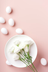 The concept of Easter table setting, white flowers lie on a white plate, next to white eggs on a powdery background, vertical orientation, copy space