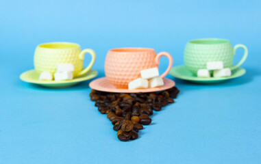 It's coffee time. yellow orange and green  coffee cups on the table.There are coffee beans and sugar on the tablend.