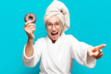 senior pretty woman after shower and wearing bathrobe and having breakfast with a donut