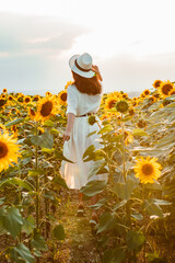 young woman in sundress walking by sunflowers field on sunset