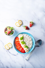 Oatmeal porridge with milk and fresh strawberries and banana slices in a blue bowl