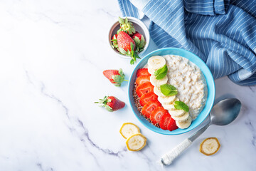 Oatmeal porridge with milk and fresh strawberries and banana slices in a blue bowl
