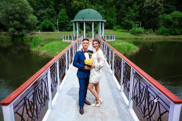 Stylish groom with his beloved beautiful wife, short wedding dress, romantic and cheerful couple in the park near the gazebo