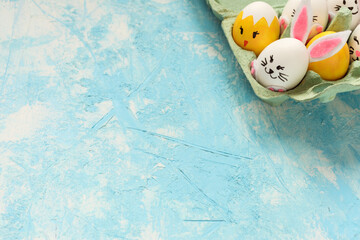 Beautiful Easter background, Easter eggs painted as bunnies and chicks in the egg carton on the light blue background. Copy space. 