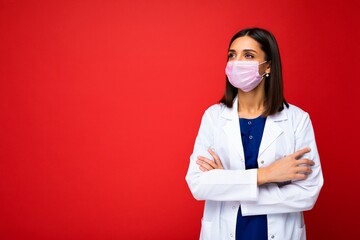 Young beautiful brunette woman in virus protective mask on face against coronavirus and white medical coat isolated on the background