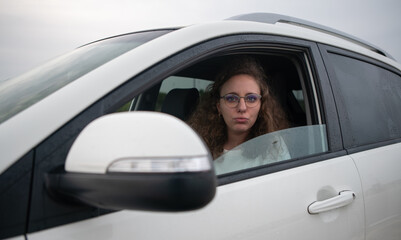 Sad and overwhelmed woman inside her white car while waiting in a traffic jam.