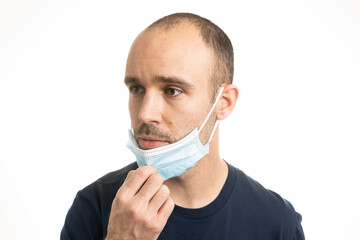 A white Caucasian male wearing a blue t-shirt and adjusting a blue surgical mask with a neutral expression and showing his mouth.