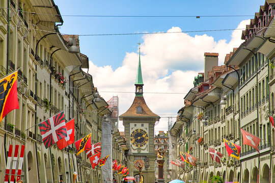 Bern, Switzerland - Aug 23, 2020: Kramgasse street with Swiss flags and Zytglogge Clock Tower and Zahringerbrunnen and Simsonbrunnen fountains.