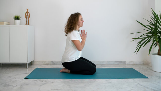 Young woman practicing yoga and doing the Namaste salute on a blue mat at home.