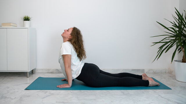Young woman practicing yoga postures on a blue mat at home.