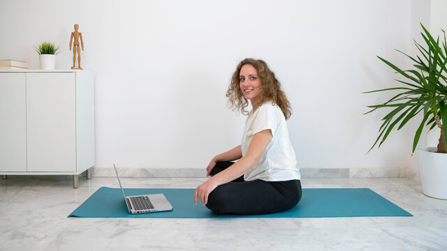 Woman with curly blond hair practicing a yoga class with her computer from home.