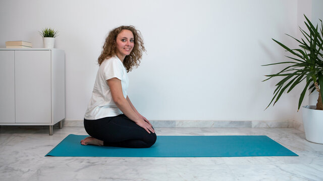 Young woman similing and practicing yoga postures on a blue mat at home.
