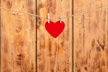 A red heart hangs on a string. In the background is a wooden background. Selective focus on the heart.