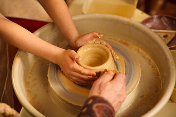 A close-up of the hand of a male potter who teaches his pupil, a child of the art of making a pot or a vase of clay. People working on potters.
