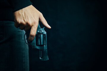 Guy with gun down. Black revolver with drum in man's hand. Firearms for attack or defense. Armed person on dark background. - obrazy, fototapety, plakaty