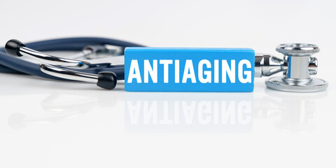 On a white reflective surface is a stethoscope and a blue Jenga with the inscription - ANTIAGING