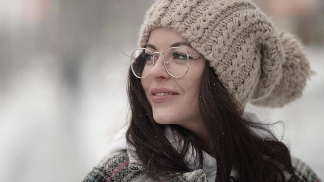 charming young woman with glasses and nice knitted hat is walking at winter, closeup portrait