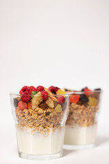 muesli dessert with yogurt and candied or dried fruits with raspberries on top in glass isolated on white background. Granola breakfast