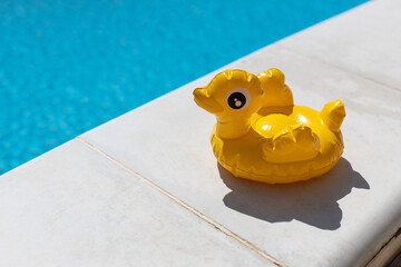 Inflatable yellow mini duck, cocktail stand near swimming pool on bright sunny day, copy space. Concept of summer vacation, entertainment, water, air, sunbathing, health. Side view. Horizontal