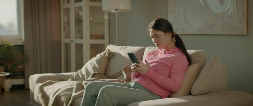 WIDE Portrait of Asian Korean female checking her phone at home early in the morning. Natural cinematic light. Shot with 2x anamorphic lens