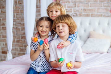 Easter children portrait, funny emotions, surprise. Children, a girl and two boys hold Easter eggs in their hands. Funny photo. Adorable kid in colored clothes enjoying holiday