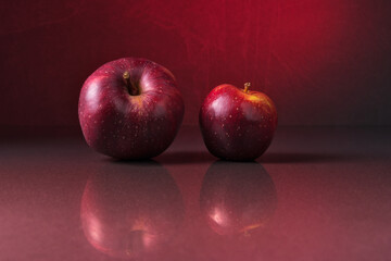 Big and small red apples on stone background with reflection