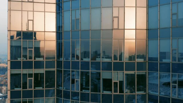 Aerial elevator shot of a modern glassed office skyscraper exterior with cityscape reflection in the windows at sunset or dawn