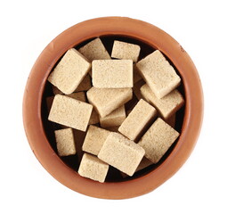 Brown cane sugar cubes in clay pot isolated on white background, top view