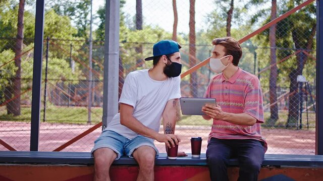 In the quarantine two guys studying together in the park at fresh air they using a electronic tablet to analyzing some documents then continue to discussing concept of Coronavirus