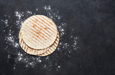 Grilled tortilla. Mexican flatbread - tortilla on a black concrete background with flour.
